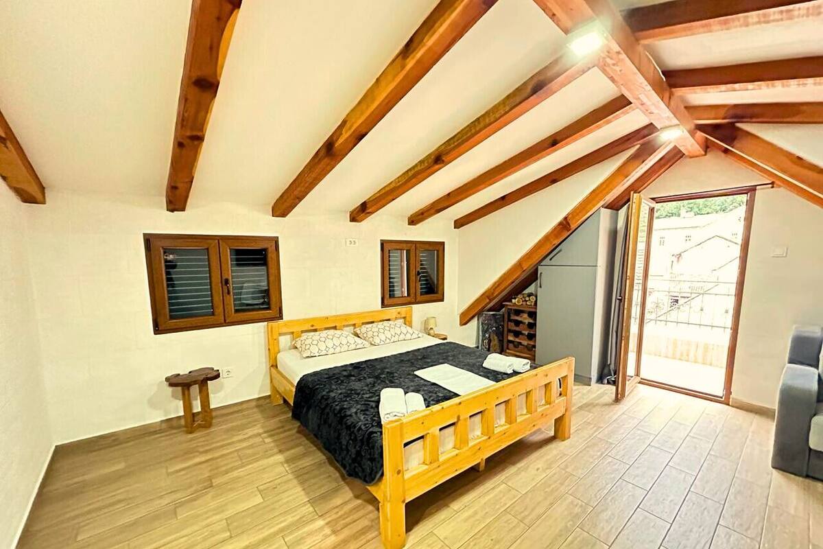 A bedroom with a wooden bed, a small stool, and a door leading to a balcony.