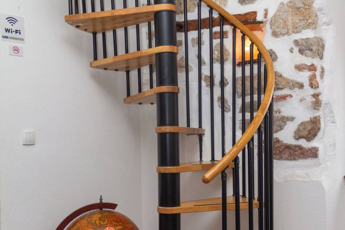 A spiral staircase with wooden steps and black railings, a globe on a pedestal, and a stone wall.