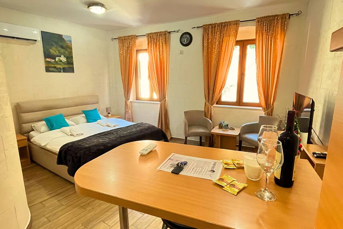 A hotel room with a bed, a desk, a chair, a small table, and a window with curtains.