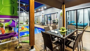 A modern indoor pool area with a glass table and wicker chairs, surrounded by large windows and a cozy seating area. - OC Breeze Casa Private Pool Villa With 3 Bedrooms, Near Cha-am Beach (Cha-am)