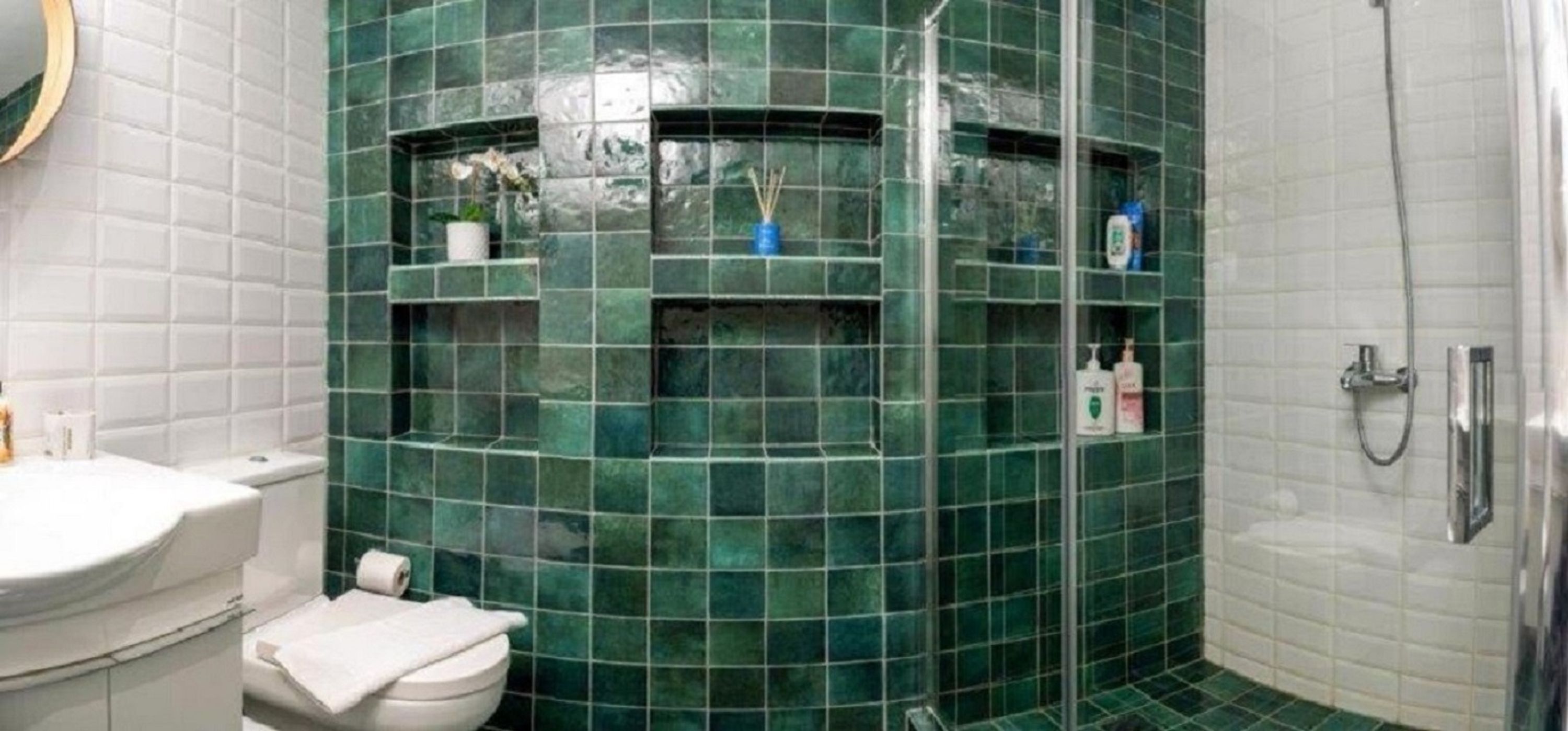 Une salle de bain avec un mur incurvé recouvert de carreaux verts, un lavabo blanc, des toilettes et un espace douche.