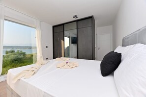 A modern bedroom with a large bed, a view of the outdoors, and a wardrobe. - Villa Giovanni Zadar Villas (Razanac)