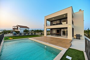 A modern two-story house with a swimming pool, outdoor seating, and a view of the mountains. - Villa Giovanni Zadar Villas (Razanac)