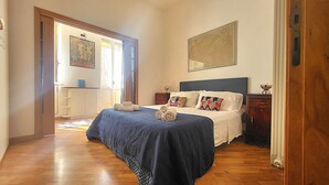 Una camera da letto con un letto, un comodino, una cassettiera e una porta che dà su un'altra stanza.