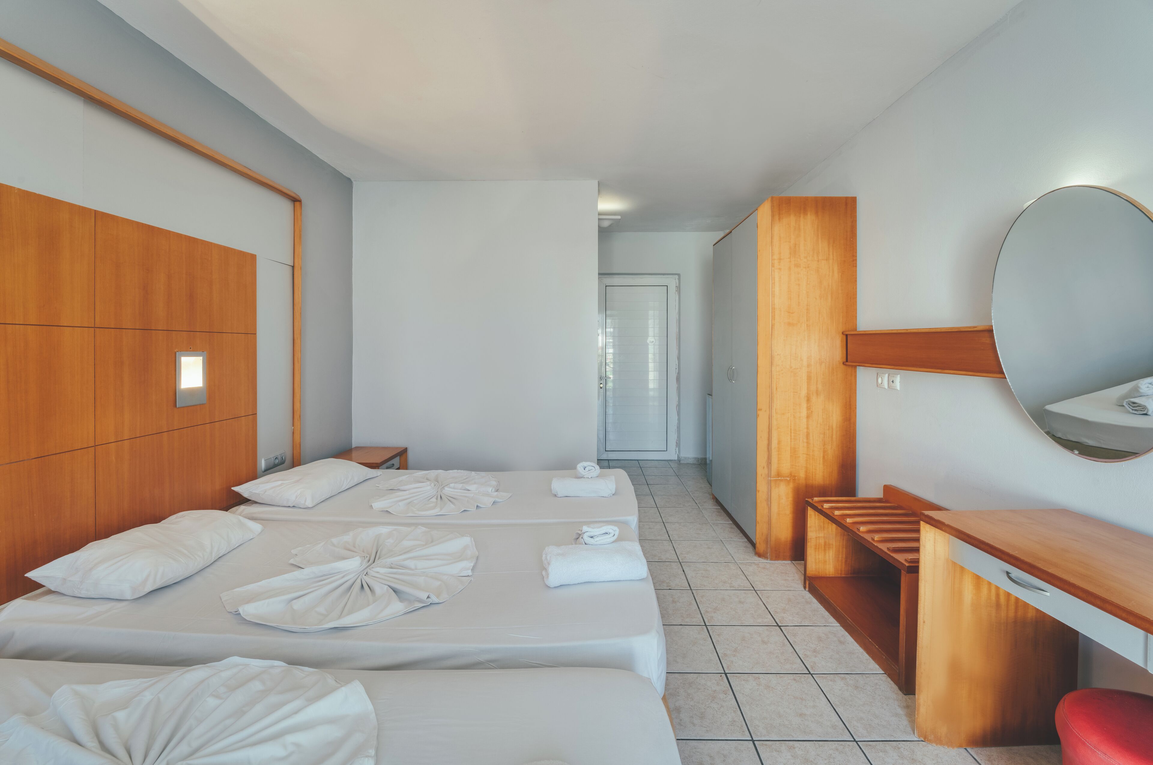 A hotel room with two beds, a wooden wardrobe, a desk, and a mirror.