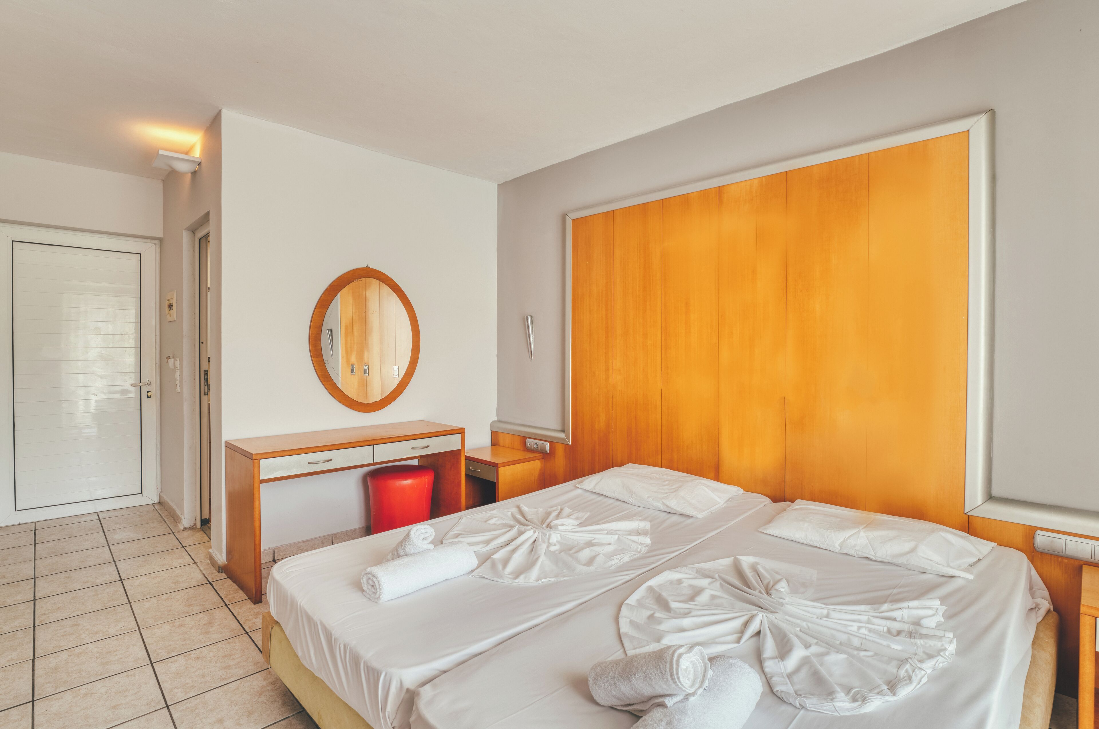 A hotel room with a large bed, a wooden headboard, a small desk with a mirror, and a red trash bin.