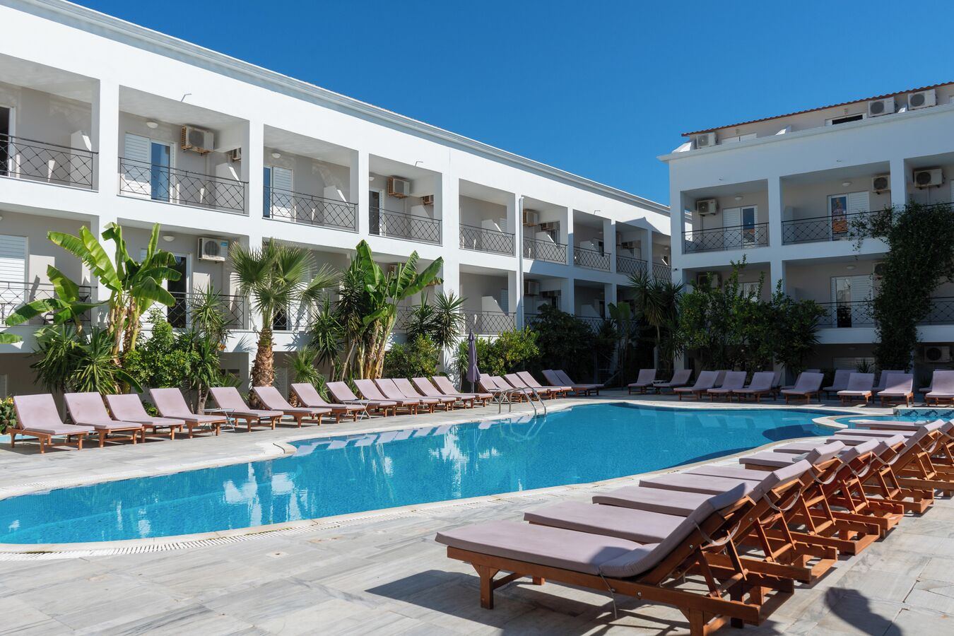 Zona junto a la piscina con sillones reclinables y una piscina, rodeada por un edificio de varios pisos con balcones.