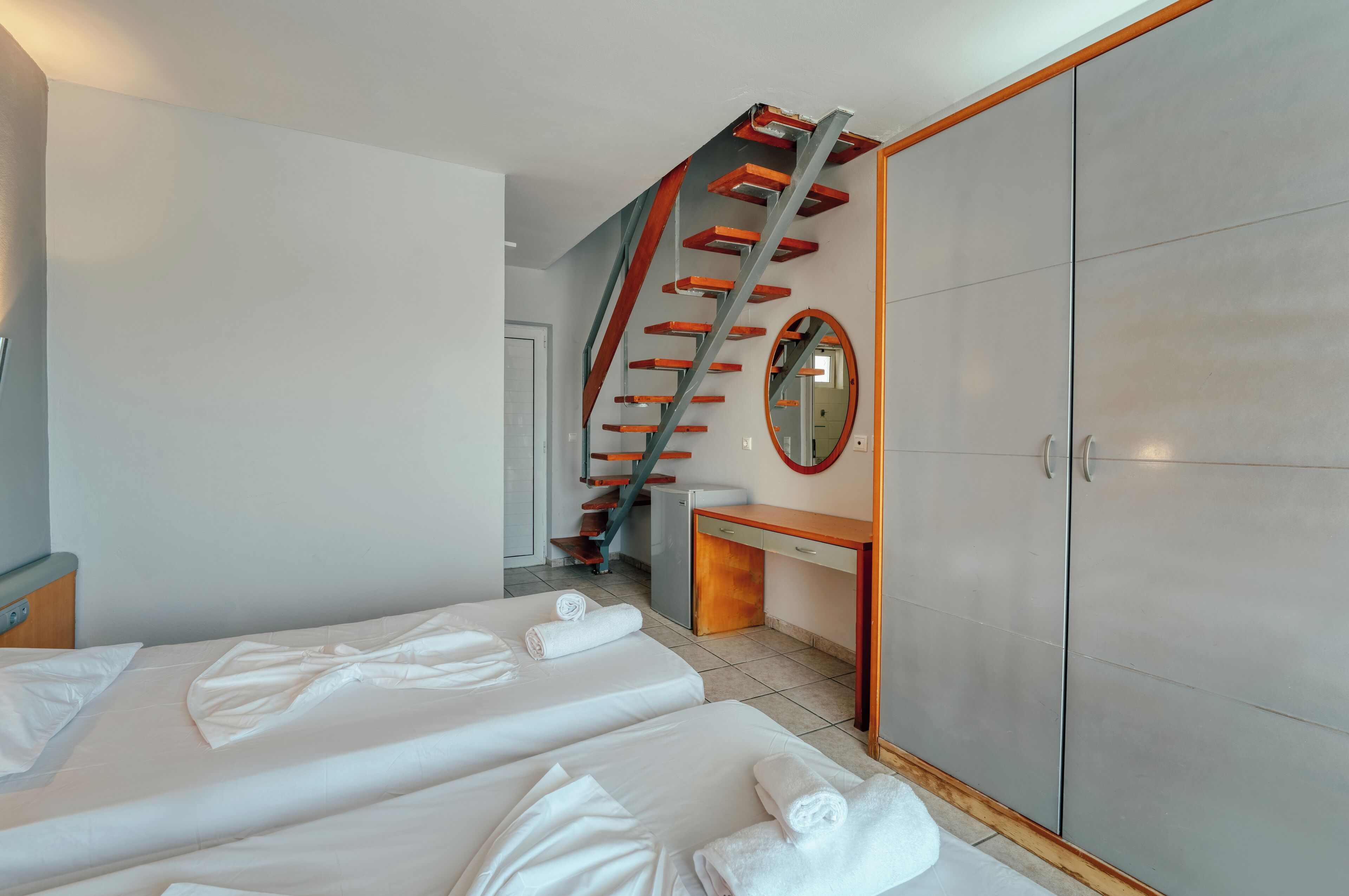 Une chambre d’hôtel avec deux lits, un bureau, une armoire et un escalier en colimaçon.