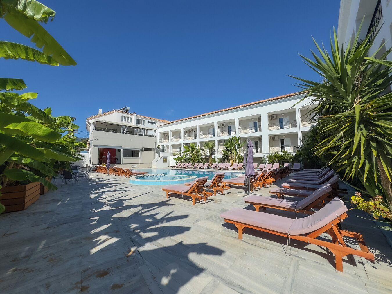 A poolside area with lounge chairs and a pool, surrounded by a building with multiple balconies and air conditioning units.
