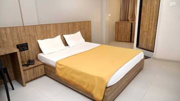 A neatly made bed with a wooden headboard, a bedside table with a phone, and a yellow blanket.