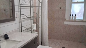 A bathroom with a shower, toilet, vanity, and a window with bottles on the sill. - Charming Highlands Gem - Classic 3BR Retreat (Louisville)
