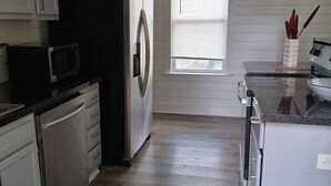 A kitchen with white cabinets, a stainless steel refrigerator, a microwave, and a stove. - Charming Highlands Gem - Classic 3BR Retreat (Louisville)
