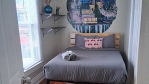 A bedroom with a bed, a window with blinds, a wall-mounted shelf, and a painting. - Charming Highlands Gem - Classic 3BR Retreat (Louisville)