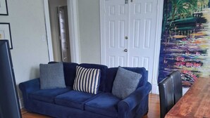 A living room with a blue sofa, a wooden dining table, and a red patterned rug. - Charming Highlands Gem - Classic 3BR Retreat (Louisville)