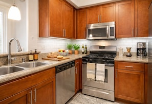 A modern kitchen with wooden cabinets, stainless steel appliances, a granite countertop, and a potted plant. - 1-Bedroom Paradise Stay Close To Venice (Marina del Rey)