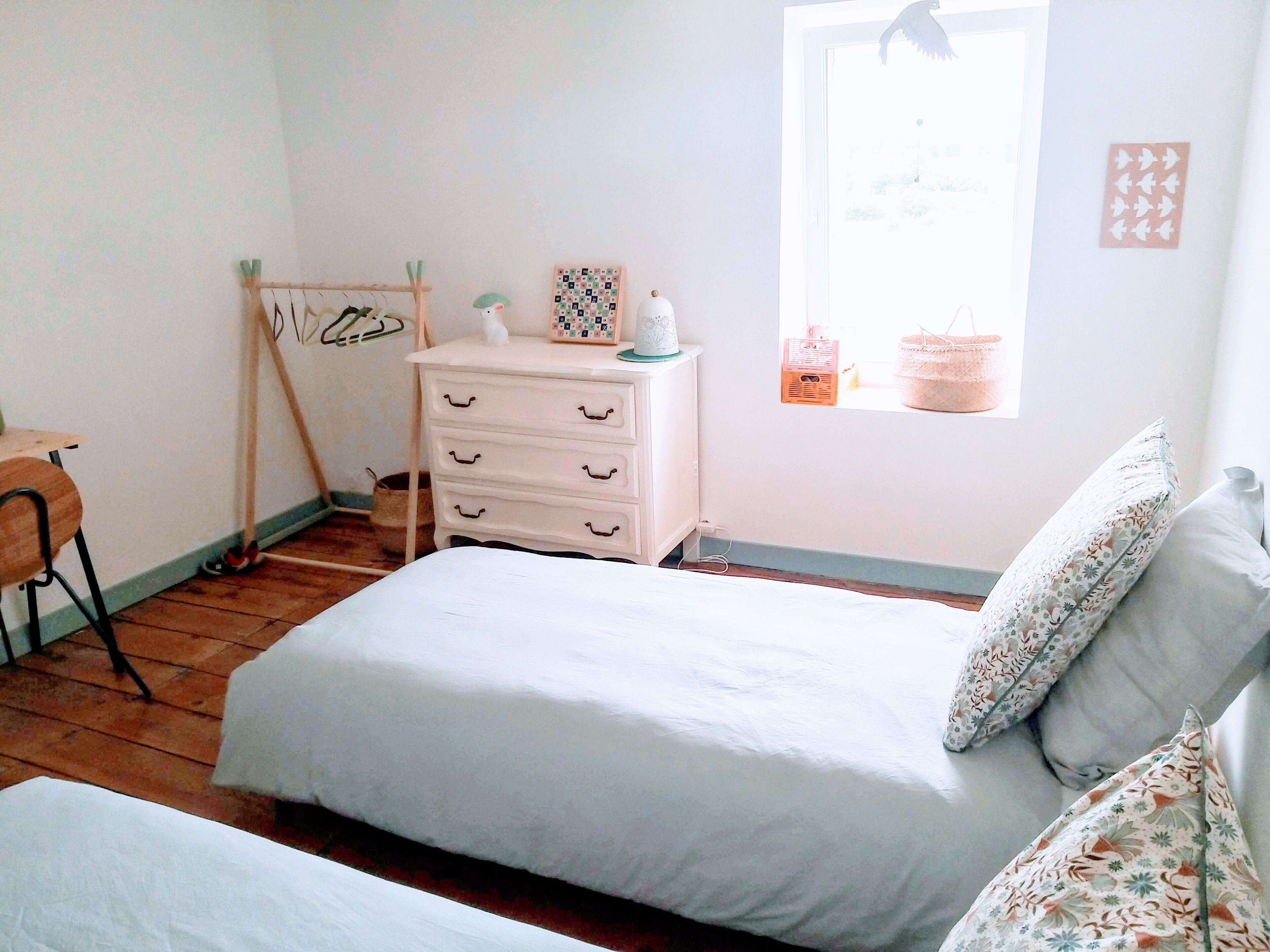 Ein Schlafzimmer mit Bett, Kommode, Fenster mit Blick und Stuhl.