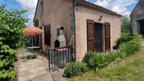 Edifici rústic amb un patio de pedra, una taula petita i un para-sol vermell.