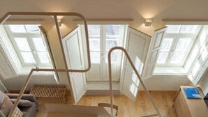 Une pièce aux hauts plafonds, dotée de lucarnes, d’un plancher en bois et d’un escalier avec des rampes en métal.