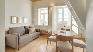 Un salon chaleureux avec un canapé, une table ronde et des chaises. Il y a de grandes fenêtres et un plafond en pente.