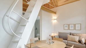 Un salon moderne avec une table à manger ronde en bois, un canapé et un escalier en colimaçon blanc.