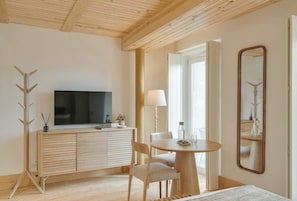 A modern room with a wooden ceiling, a flat-screen TV on a wooden cabinet, a round dining table with chairs, a mirror on the wall, and a coat rack. - Republica 139 Apartamentos by DA'Home #2D (Porto)