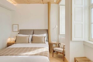 Een slaapkamer met een bed, nachtkastje, stoel en een raam met uitzicht.