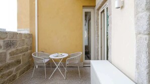 Una piccola zona esterna con due poltrone in vimini e un tavolo rotondo, vicino a un muro in pietra e a un muro giallo.