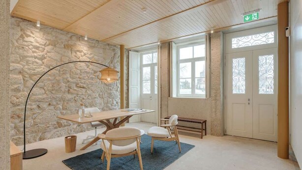 Ein geräumiger Raum mit Steinwand, Holzboden und einem großen Fenster sowie einem Tisch mit Stühlen.