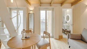 Ein modernes Wohnzimmer mit Holzbalkendecke, einem runden Esstisch mit Stühlen, einer Couch und Blick durch große Fenster.