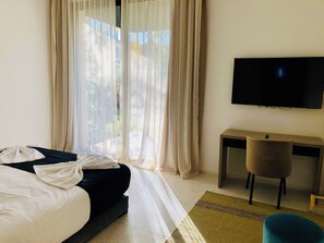 A hotel room with a bed, a TV mounted on the wall, a small desk, and a chair. - Luxury Villa in Amelkis, Marrakech: 7 Suites, Pool, Hammam, Movie Theater, View of the Atlas Mountains and Golf Course (Marrakech)