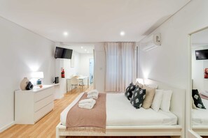 A modern hotel room with a bed, bedside table, TV, and a desk area with a chair. - Bonjardim Downtown Studio by DA'HOME (Porto)