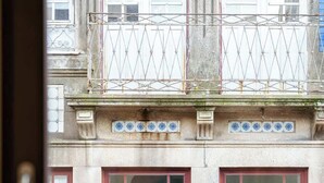 En bygnings facade med to rødlakerede vinduer, dekorativt metalgelænder og en balkon med et mønstret gelænder.