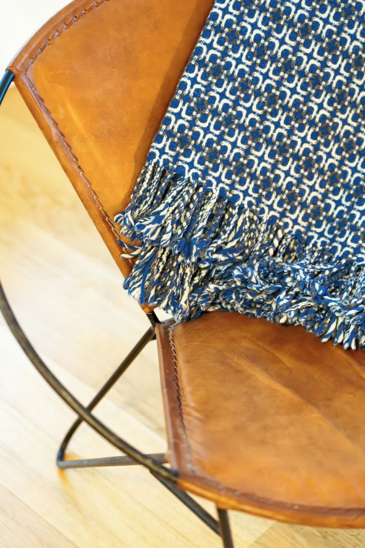 Un fauteuil en cuir marron avec un plaid bleu à motifs.