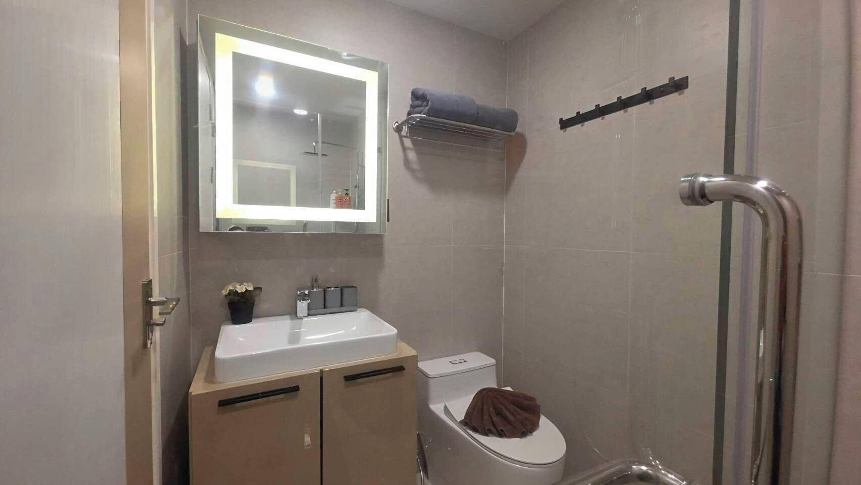 Casa de banho com lavatório, espelho, sanita e chuveiro.