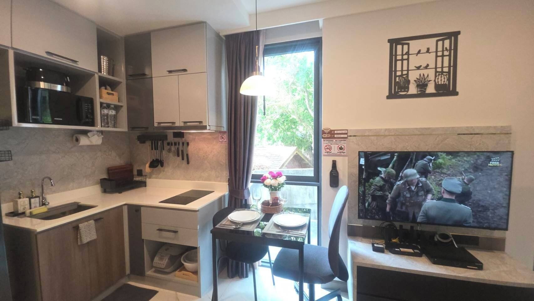 A compact kitchen with a dining area, a TV, and a window with curtains.