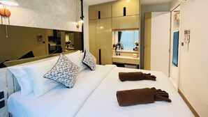 Habitación de hotel con una cama grande, dos almohadas, un espejo, un armario y un escritorio con lámpara.