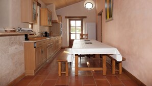 A kitchen with wooden cabinets, a dining table with benches, and a window with a view. - Gite du Pigeonnier and its tower with terraces and garden (Castelnau-sur-l'Auvignon)