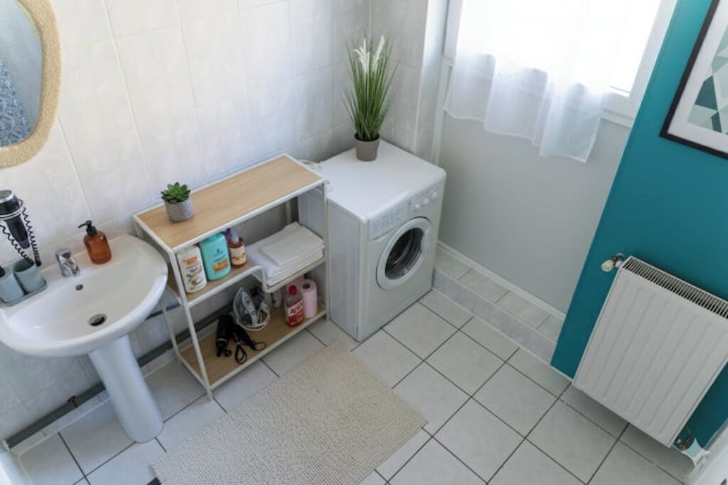 A compact bathroom with a sink, a small shelf with toiletries, a washing machine, and a radiator.