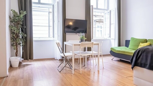 A modern living room with a TV, a dining table with chairs, a sofa, and a potted plant. - Cozy 2BR Apt With Excellent Connectivity (Vienna)