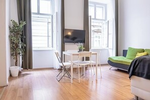 Una sala de estar moderna con una televisión, una mesa de comedor con sillas, un sofá y una planta en maceta.