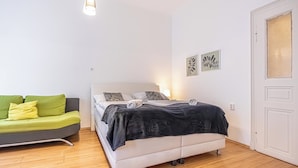 A bedroom with a bed, a green sofa, and a white door. - Cozy 2BR Apt With Excellent Connectivity (Vienna)
