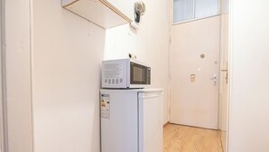 A compact kitchen with a white refrigerator and microwave, a wooden floor, and a closed door in the background. - Cozy 2BR Apt With Excellent Connectivity (Vienna)