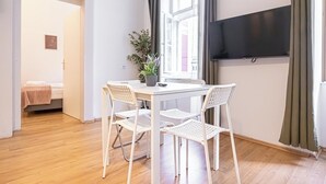 A room with a white table and chairs, a potted plant, a flat-screen TV, and a window with curtains. - Cozy 2BR Apt With Excellent Connectivity (Vienna)