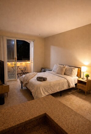 A bedroom with a bed, a nightstand, a lamp, and a sliding glass door leading to an outdoor area with chairs. - Cozy 1-bedroom apartment in tranquil Marina del Rey with Boardwalk Getaway (Marina del Rey)