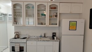 Een kleine keuken met witte kastjes, een fornuis, een spoelbak en een koelkast.