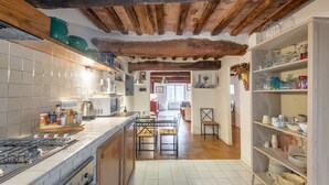 A kitchen with a tiled backsplash, wooden ceiling beams, a central island with chairs, and a dining area in the background. - Campo Apartment in the Center of Siena (Siena)