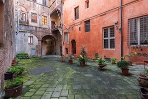 A courtyard with stone paving, potted plants, and a brick building with arched doorways. - Campo Apartment in the Center of Siena (Siena)