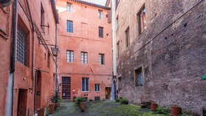 A narrow alleyway with brick buildings, potted plants, and a cobblestone path. - Campo Apartment in the Center of Siena (Siena)