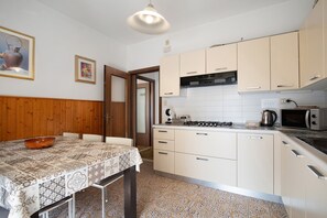 A kitchen with a dining table, chairs, a stove, microwave, and cabinets. - Apartment 'Uso Turistico' with Private Terrace, Wi-Fi and Air Conditioning (Lido di Jesolo)