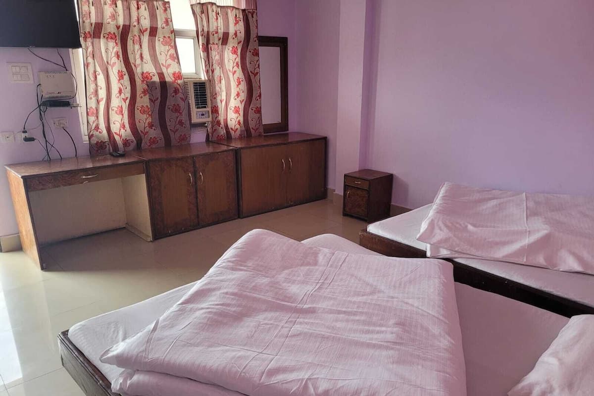 A room with two beds, a wooden dresser, a television, and a window with curtains.